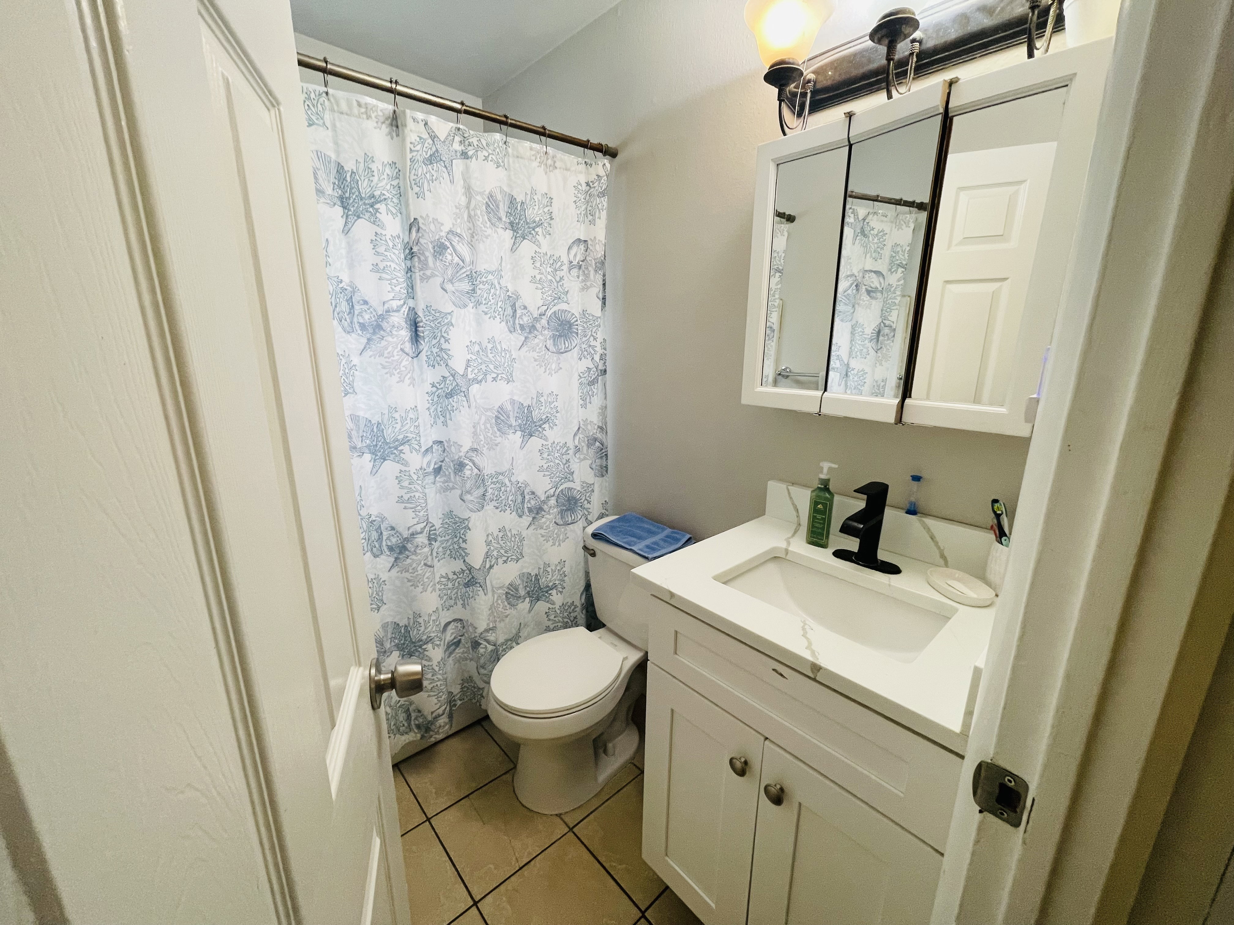 Bathroom featuring a single vanity with white cabinetry, integrated sink, black modern faucet, and a tri-fold medicine cabinet