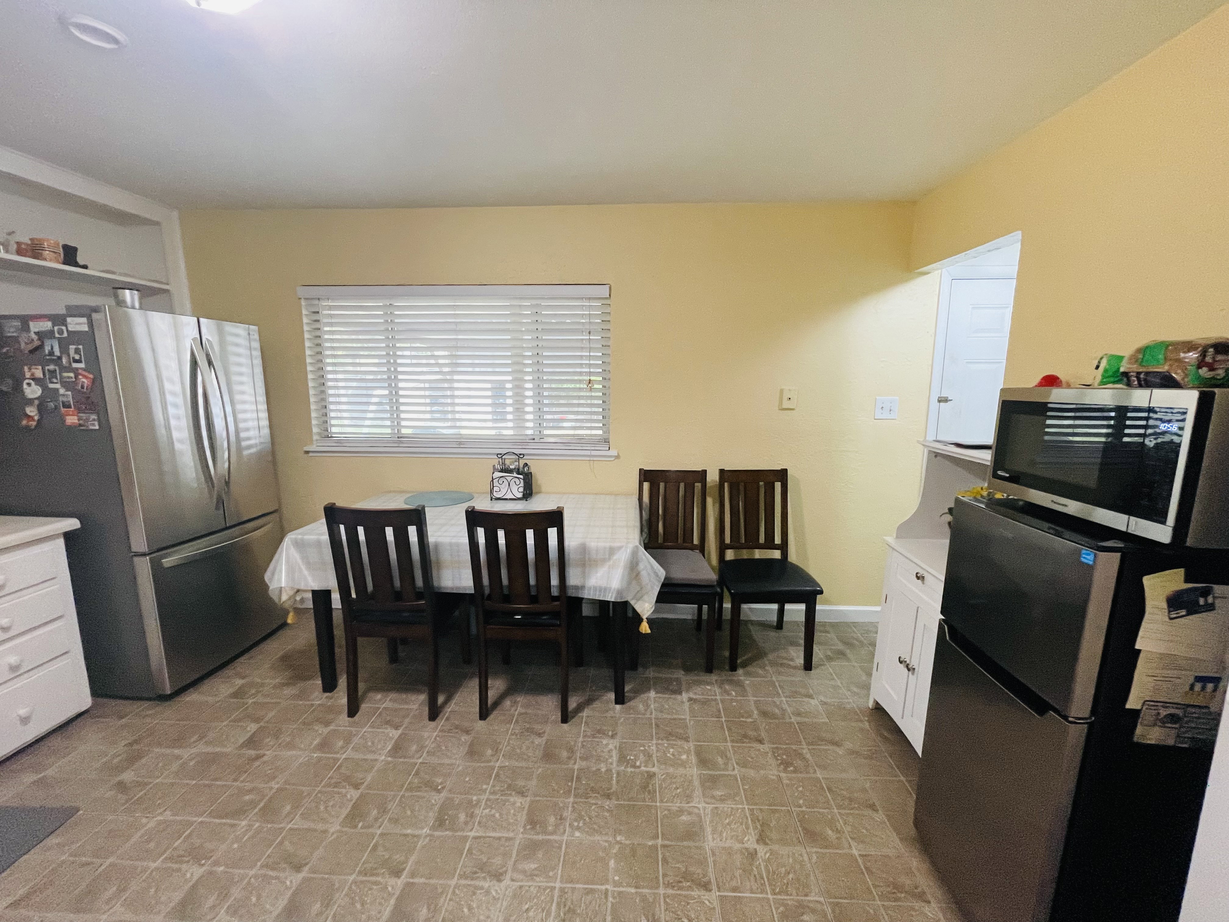 Kitchen area featuring a window with blinds, a stainless steel refrigerator, and a second stainless steel refrigerator with a microwave above it
