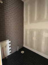Shower area featuring dark subway tile and a dark penny tile floor