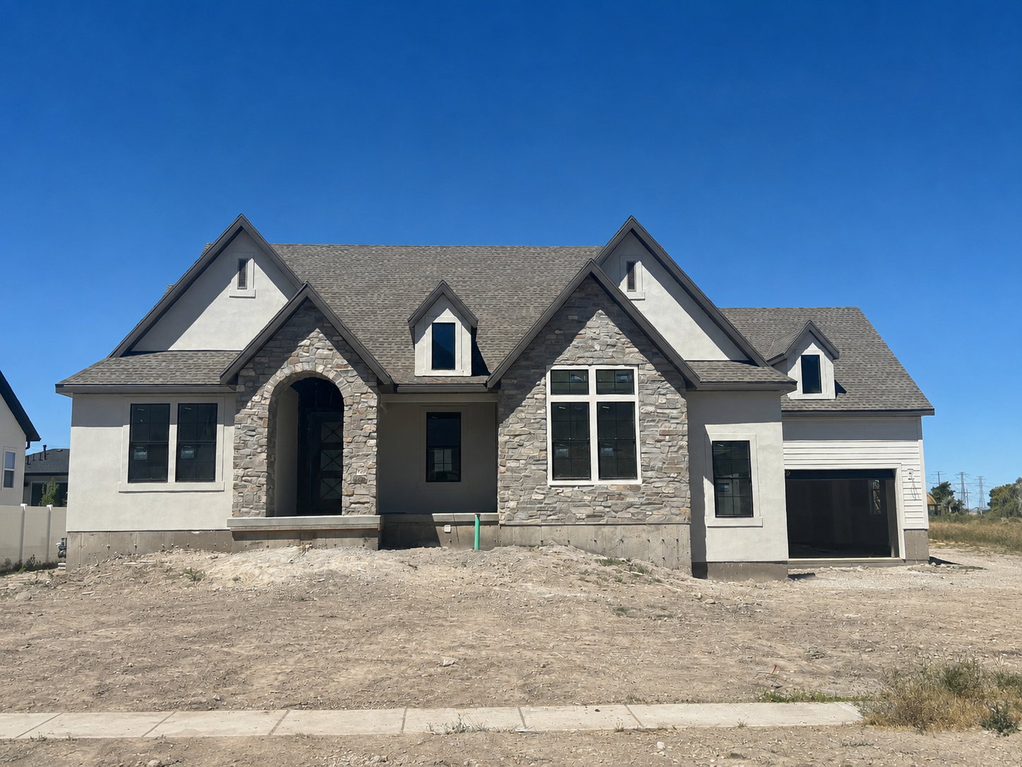 Contemporary exterior featuring a stone and stucco facade, an arched entry, a dark shingle roof, multiple dormer windows, and a two-car garage