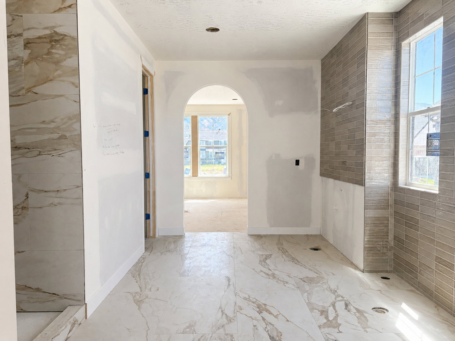 Spacious bath area featuring large format white and brown veined floor tiling, a tiled shower stall with matching veining, and a window with horizontal tile surround