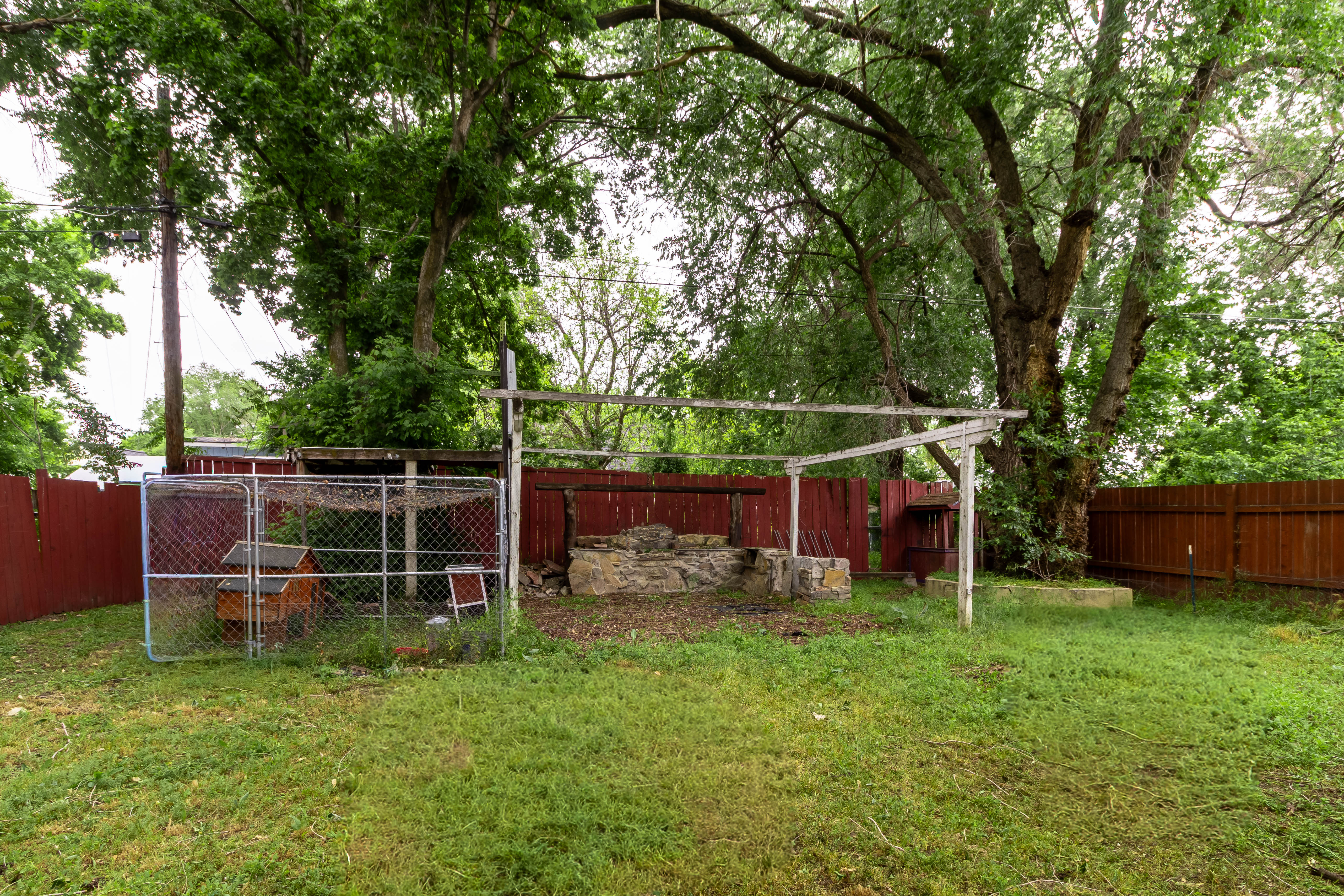 Expansive yard featuring mature trees, a red wooden privacy fence, and a chain-link enclosure