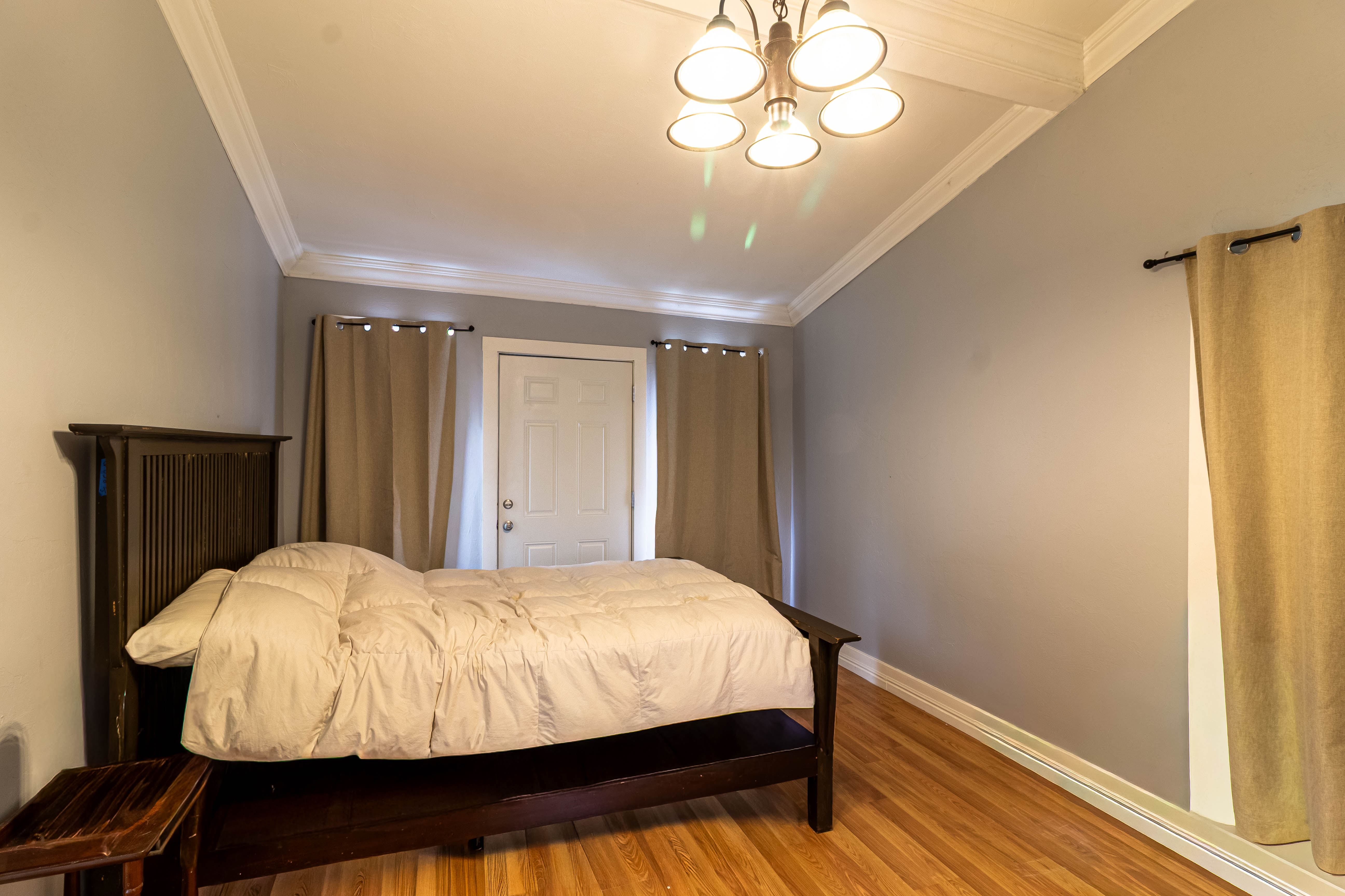 Bedroom featuring a paneled door, light wood-finish flooring, crown molding, and a five-light chandelier