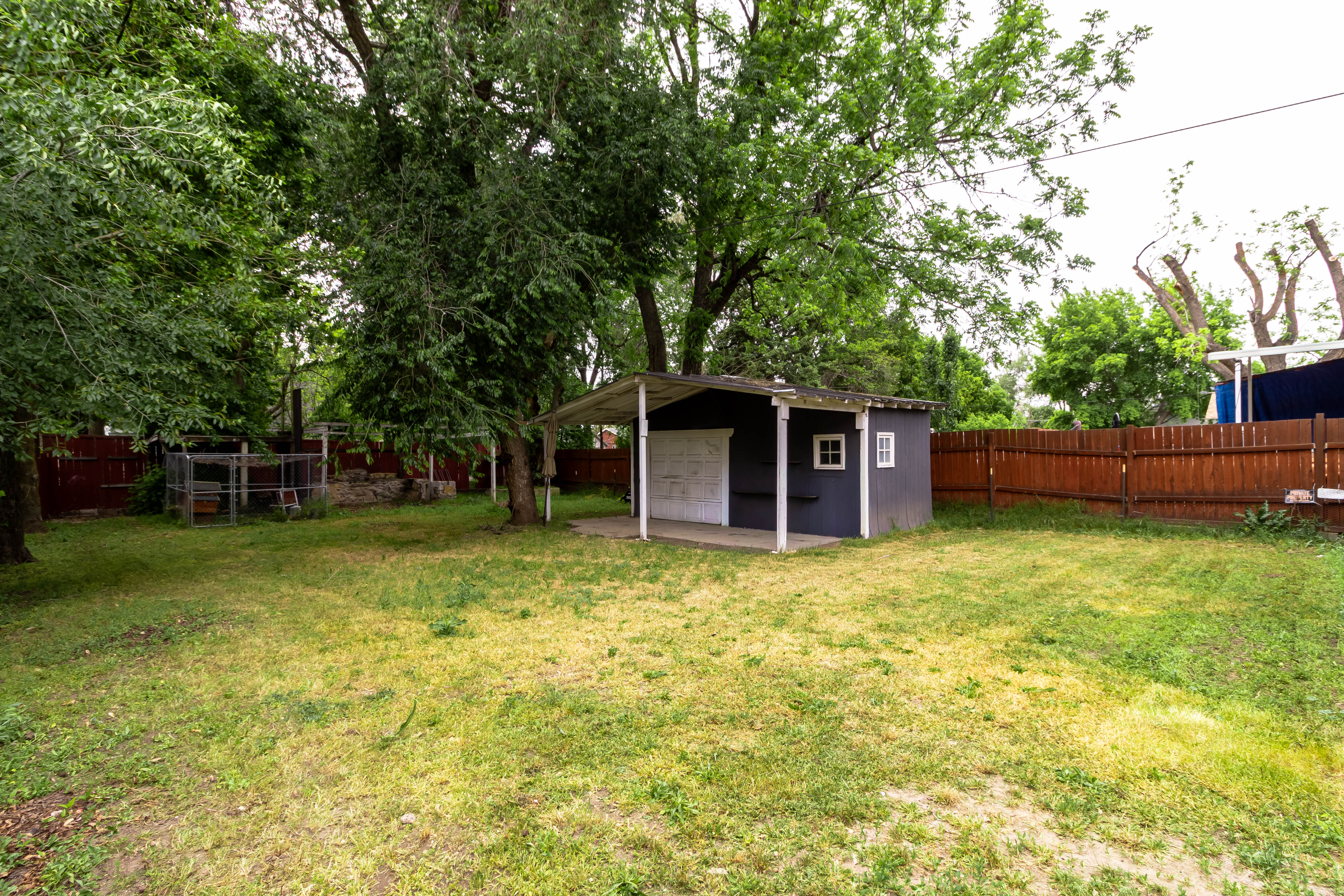 Expansive backyard featuring a detached shed with a covered porch area, mature trees, and a wood privacy fence