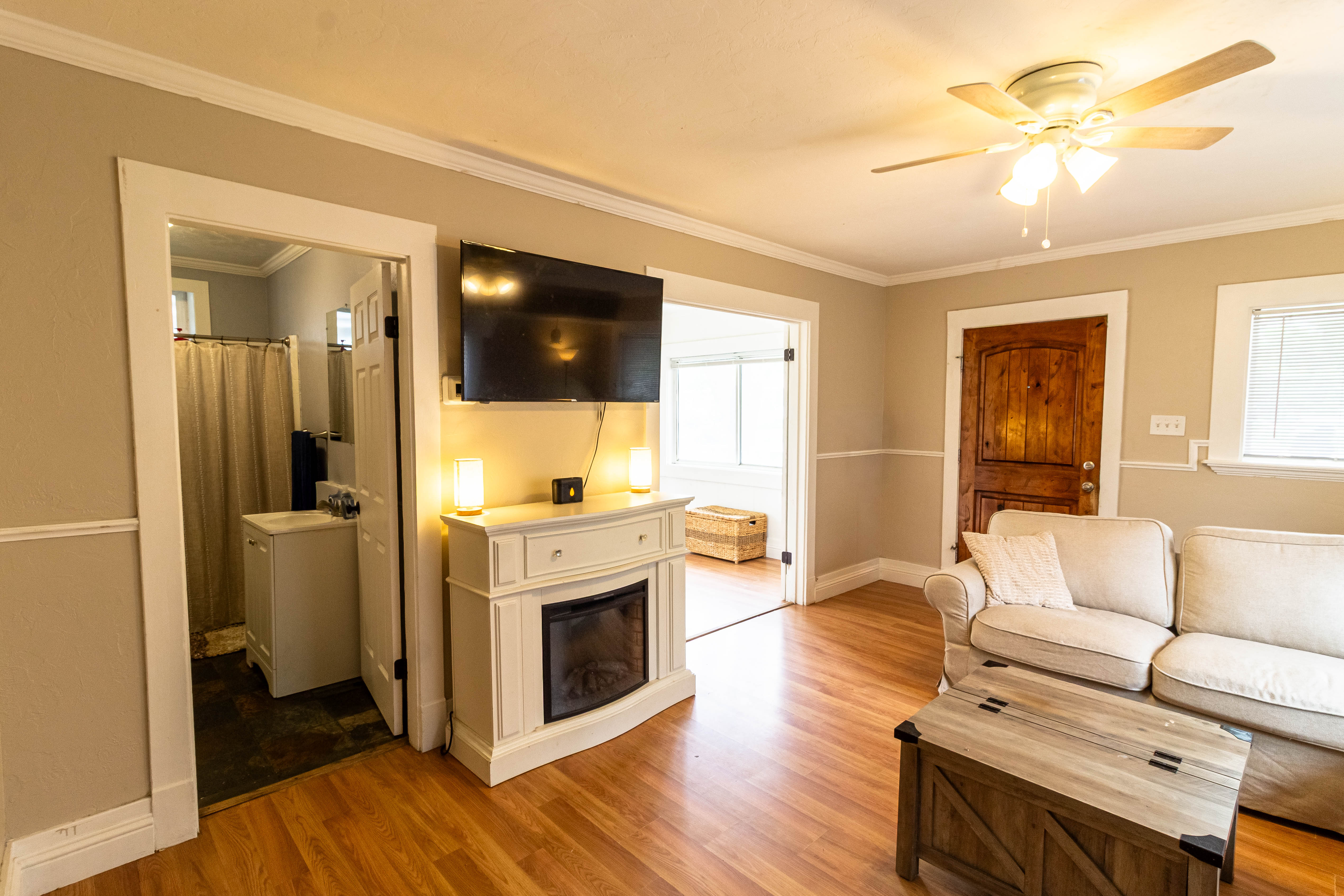 Living space featuring wood-finish flooring, an electric fireplace with a white mantel, and a ceiling fan with integrated lighting