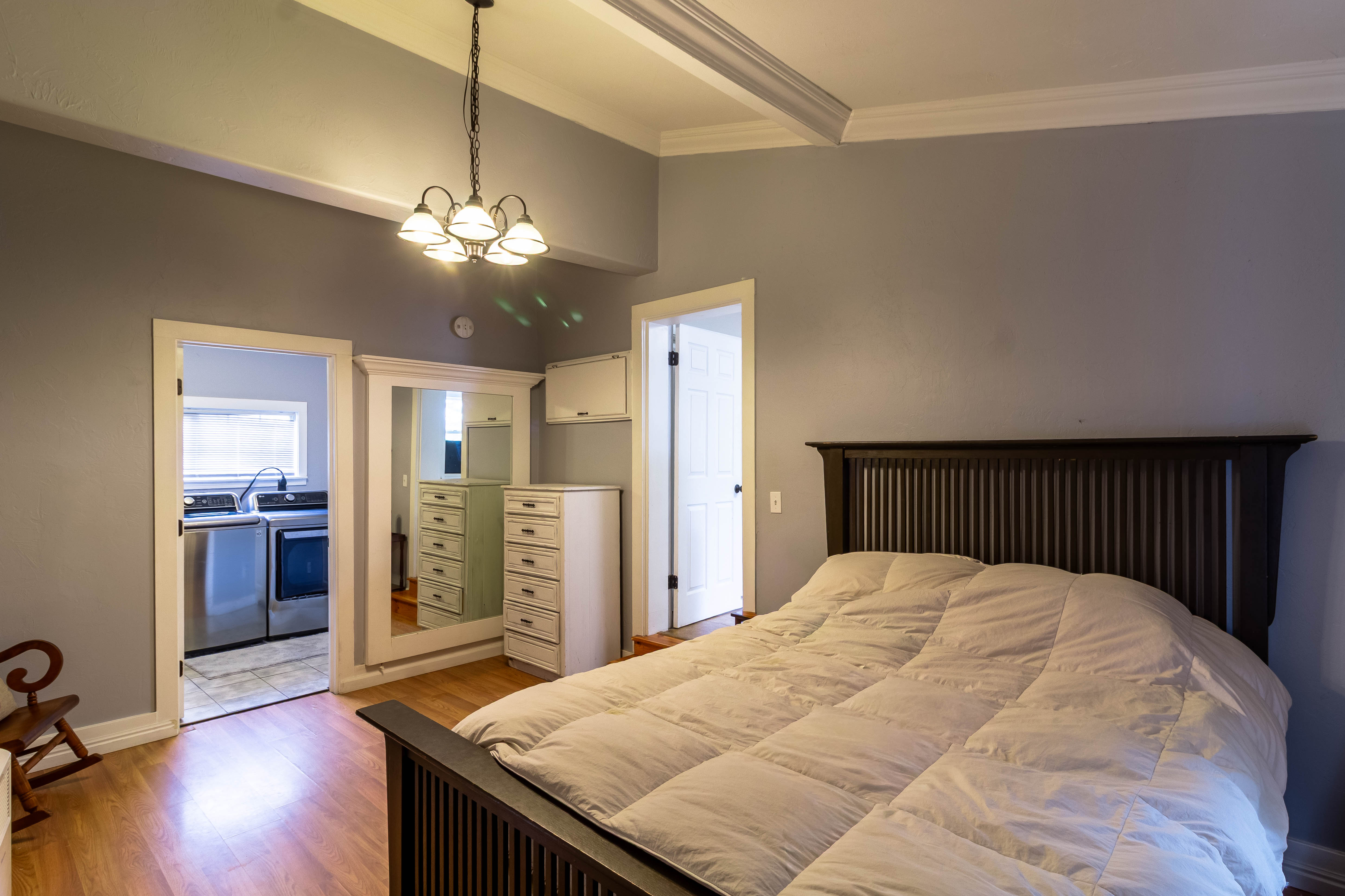 Bedroom featuring wood-finish flooring, a contemporary ceiling light fixture, crown molding, and a doorway opening to a utility space with a washer and dryer