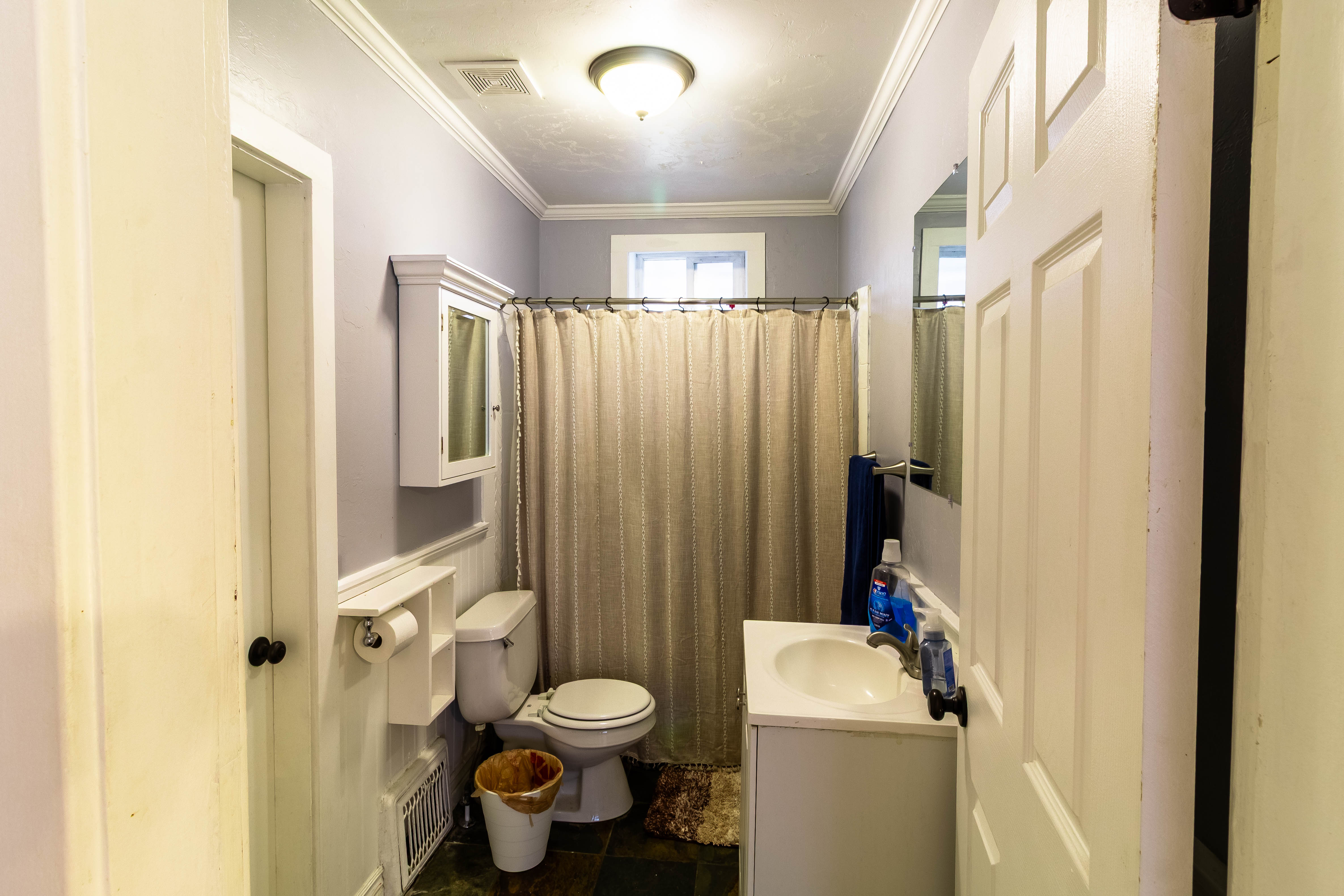 Compact bathroom featuring a single vanity, a built-in medicine cabinet, crown molding, wainscoting, and dark tile flooring