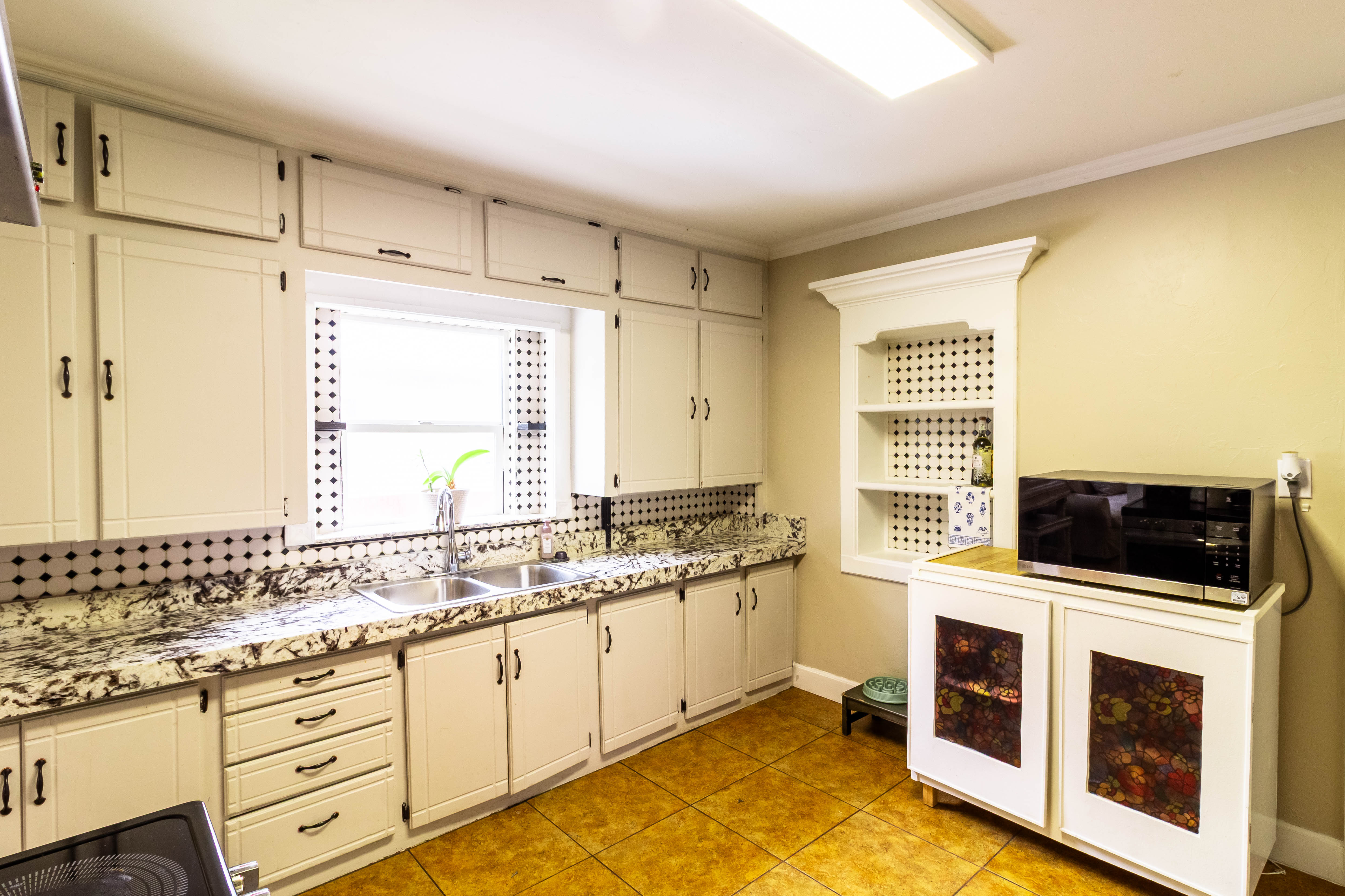Kitchen featuring extensive cabinetry, patterned countertops, a dual basin stainless steel sink, and a built-in decorative niche with shelving