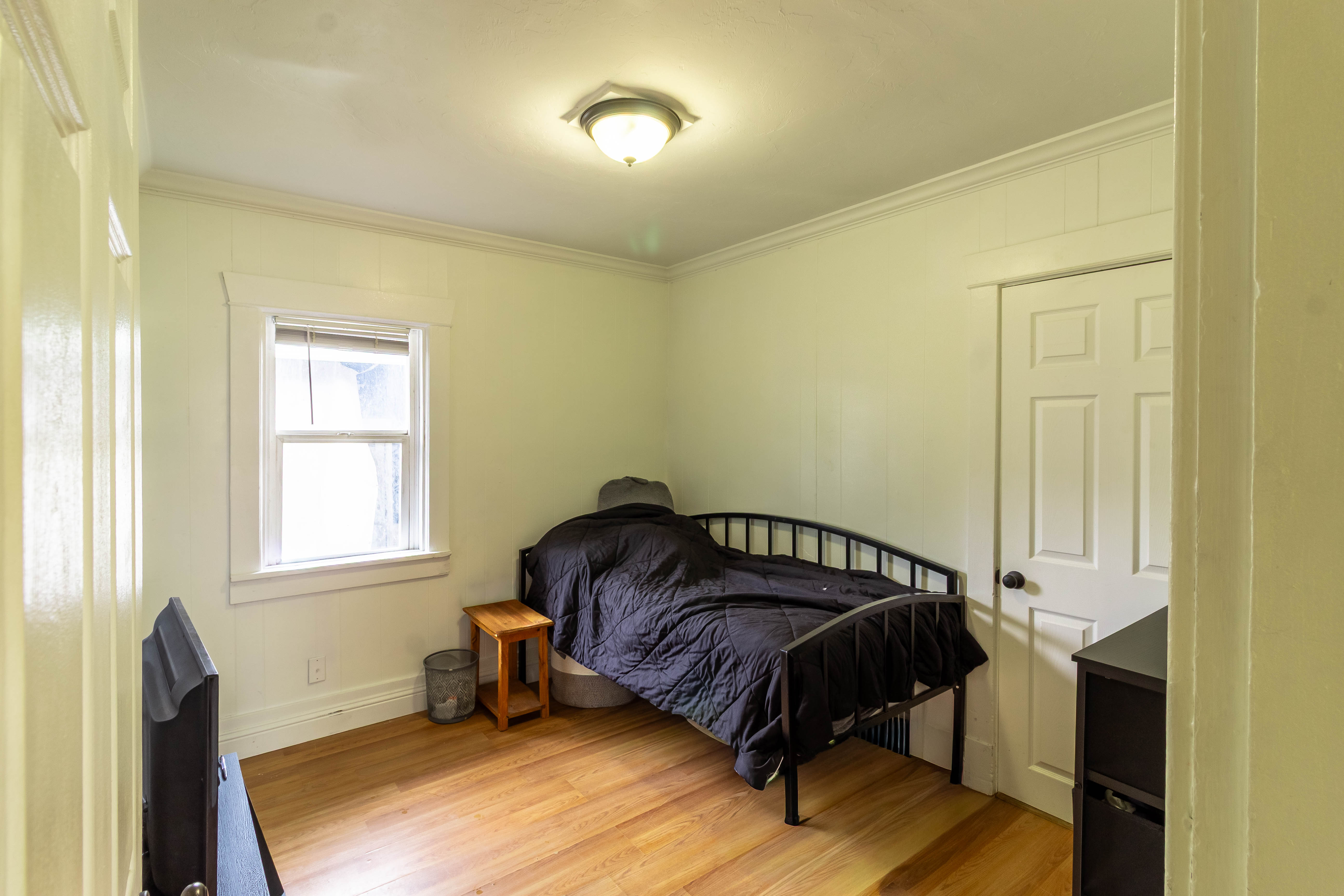 Interior room featuring wood-finish flooring, a double-hung window with white trim, and a ceiling-mounted light fixture