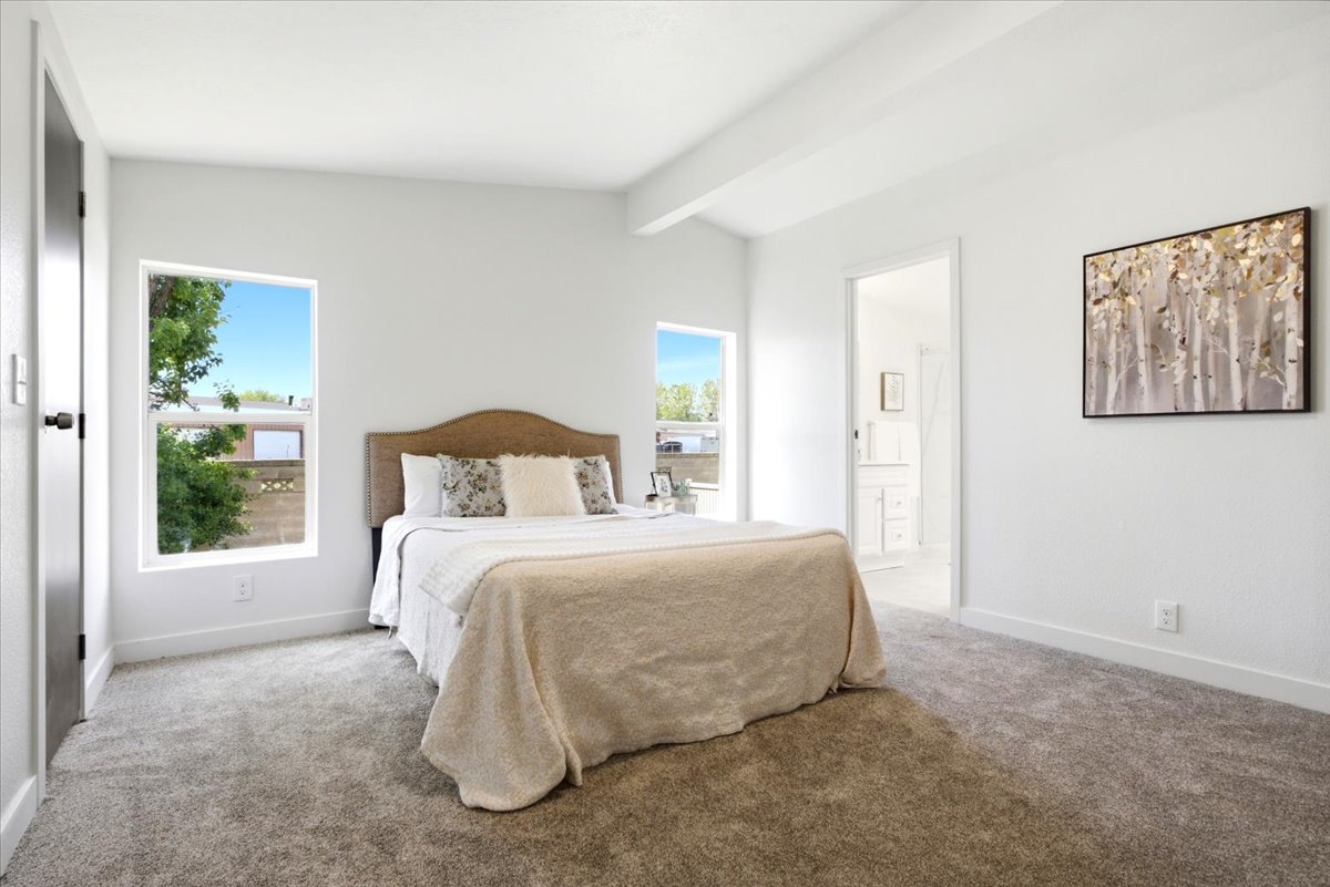 Bright room featuring two large windows, white walls, gray carpet, and a white ceiling beam
