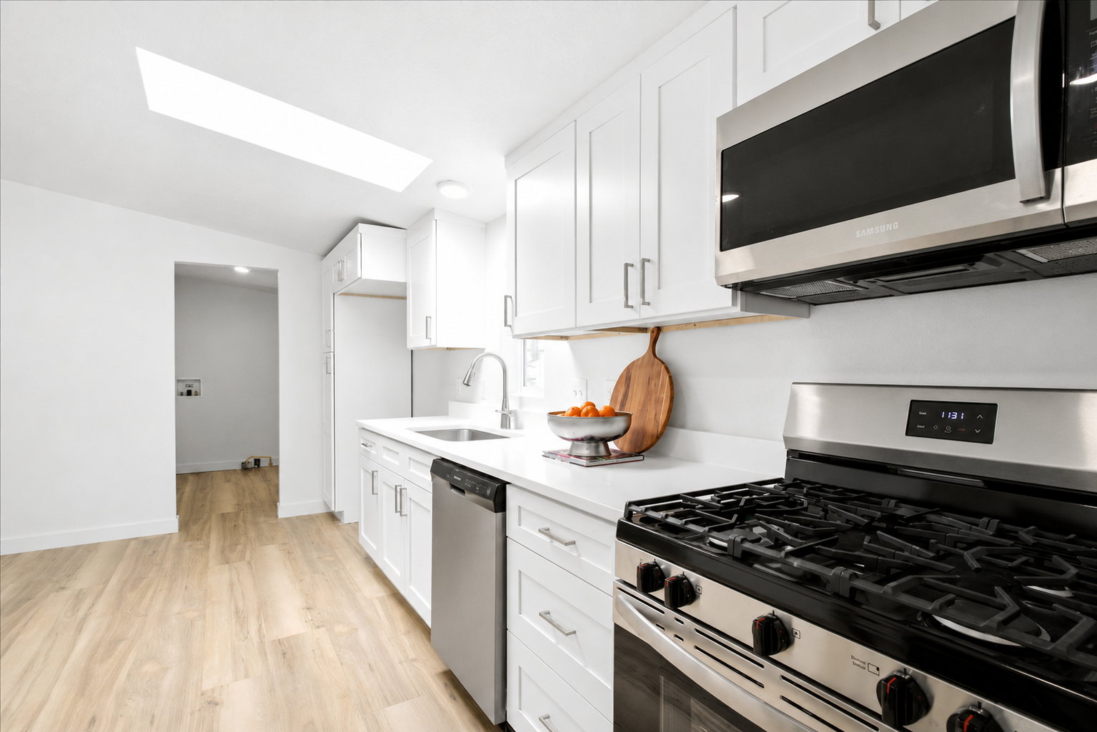 Modern kitchen featuring white cabinetry, light wood-finish flooring, stainless steel appliances, a skylight, and white countertops