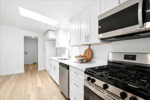 Modern kitchen featuring white cabinetry, light wood-finish flooring, stainless steel appliances, a skylight, and white countertops