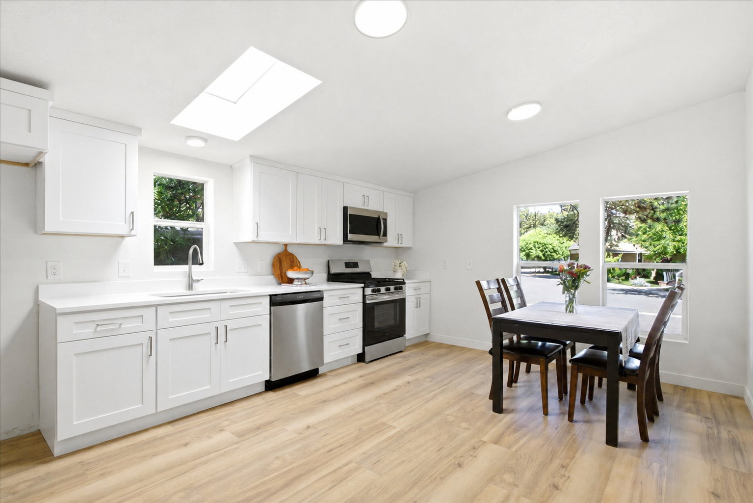 Open-concept kitchen and dining area featuring white cabinetry, stainless steel appliances, wood-finish flooring, a skylight, and recessed lighting