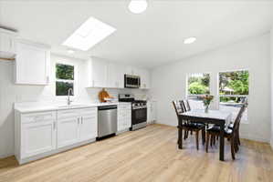 Open-concept kitchen and dining area featuring white cabinetry, stainless steel appliances, wood-finish flooring, a skylight, and recessed lighting