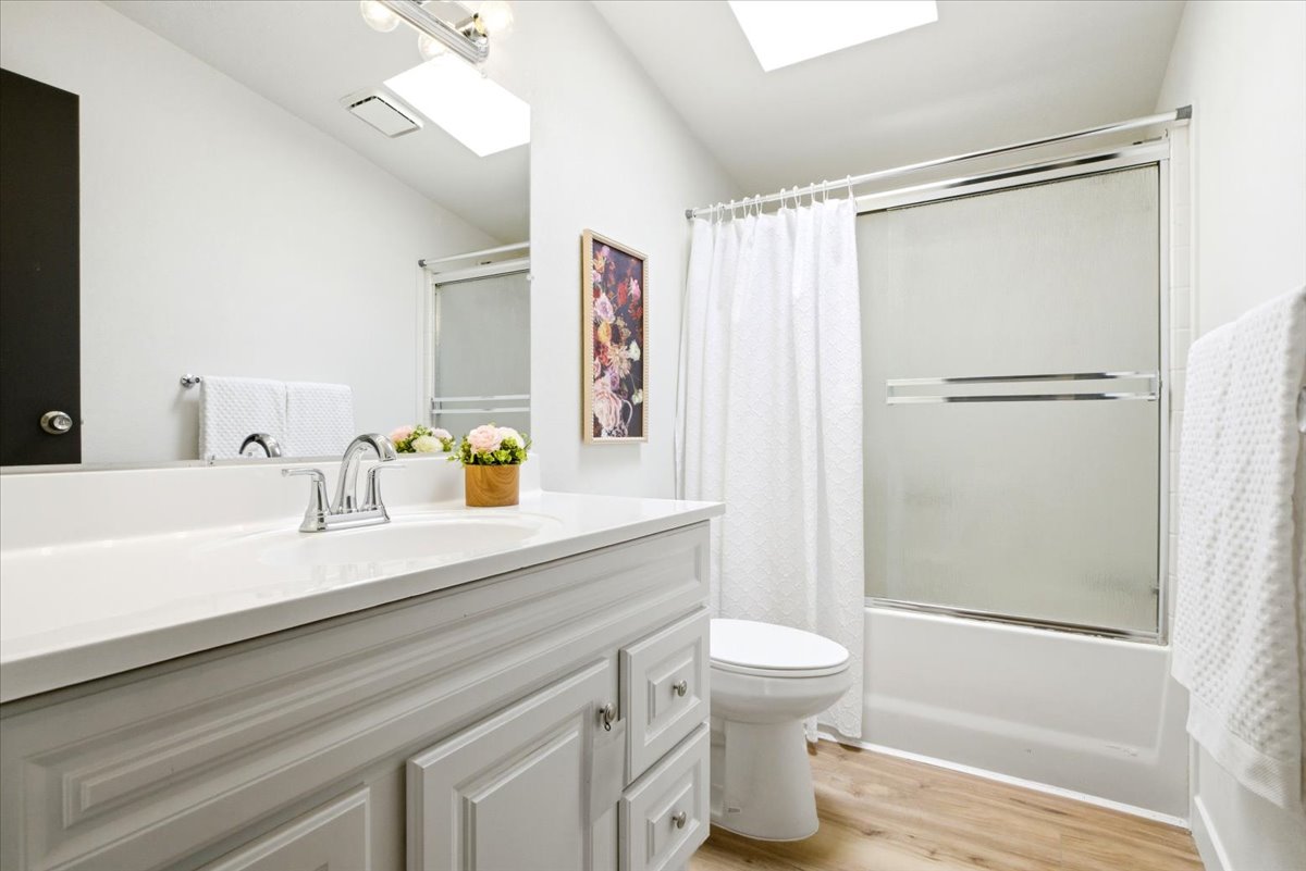 Bathroom featuring a light wood-finish floor, white vanity with an integrated sink, polished chrome faucet, and a combination tub and shower with a sliding glass enclosure