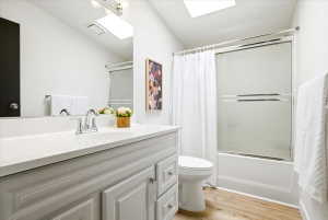 Bathroom featuring a light wood-finish floor, white vanity with an integrated sink, polished chrome faucet, and a combination tub and shower with a sliding glass enclosure