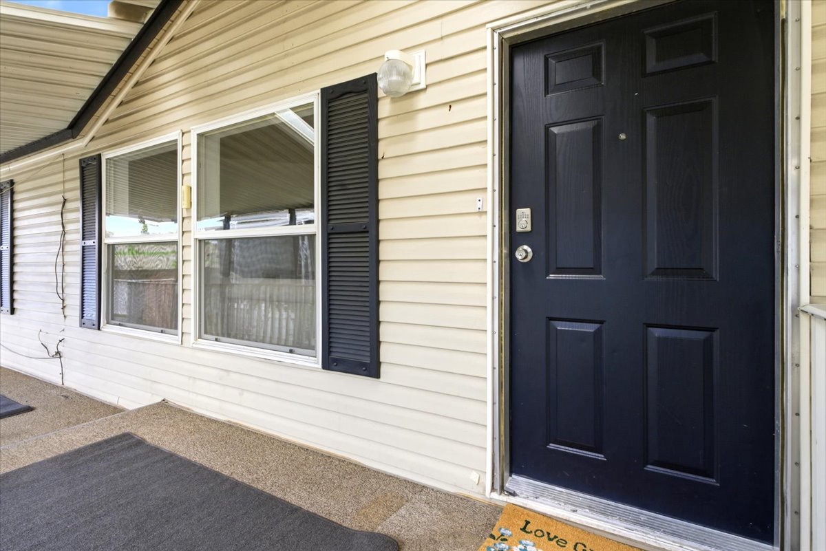 Front entry featuring a paneled door, light-colored siding, and windows with dark louvered shutters