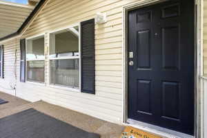 Front entry featuring a paneled door, light-colored siding, and windows with dark louvered shutters