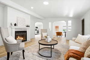 Living area featuring a fireplace with a white mantel and hearth, light-toned wood-finish flooring, recessed lighting, and arched doorways