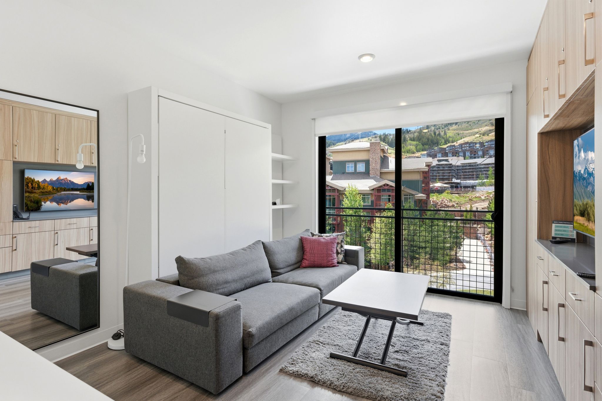 Living area featuring a sliding glass door to a balcony, wood-finish flooring, built-in cabinetry, and a wall-mounted bed