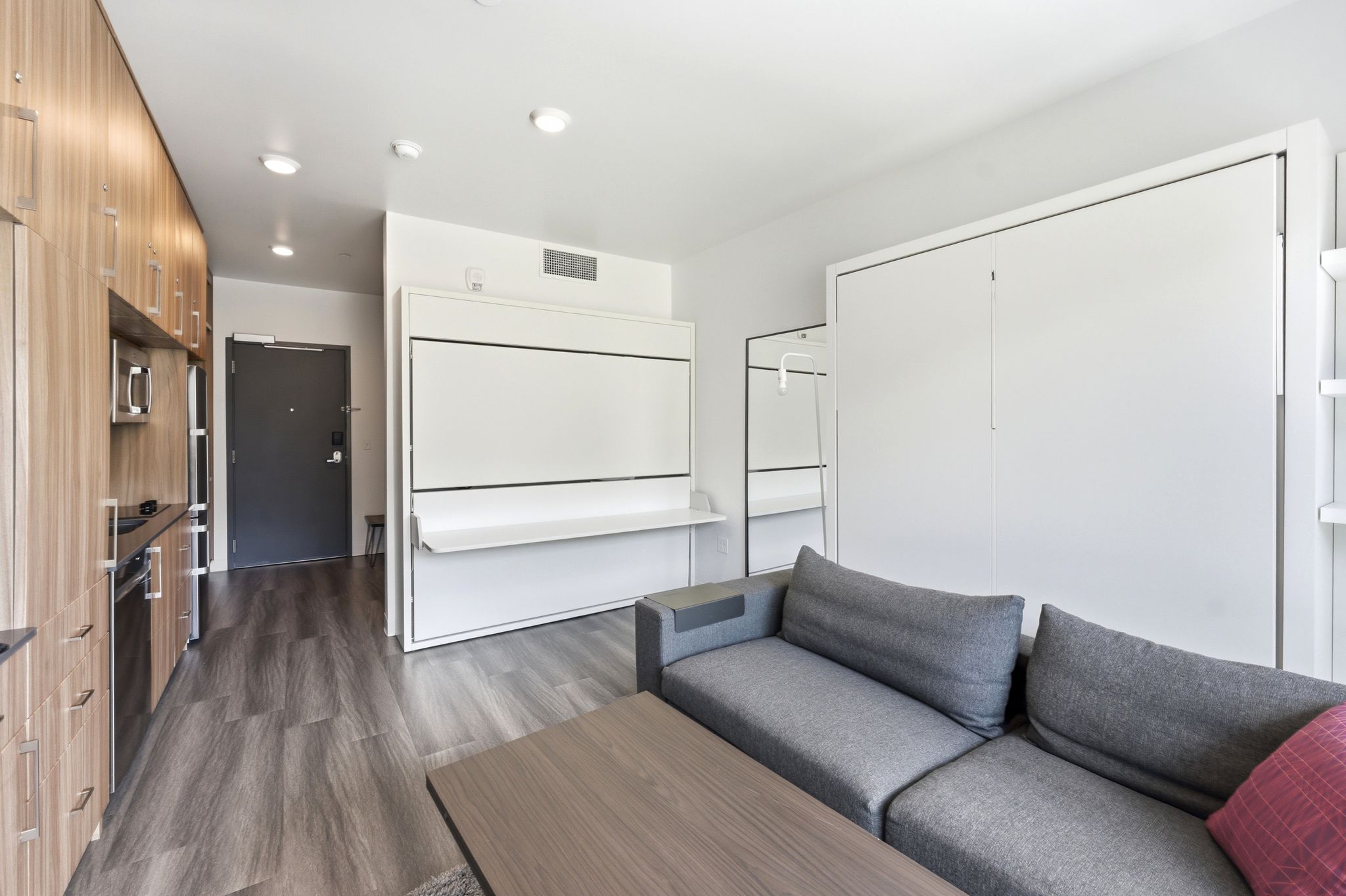 Open-concept living area featuring wood-finish flooring, a built-in wall bed system, a built-in kitchen with wood-finish cabinetry, and recessed ceiling lighting