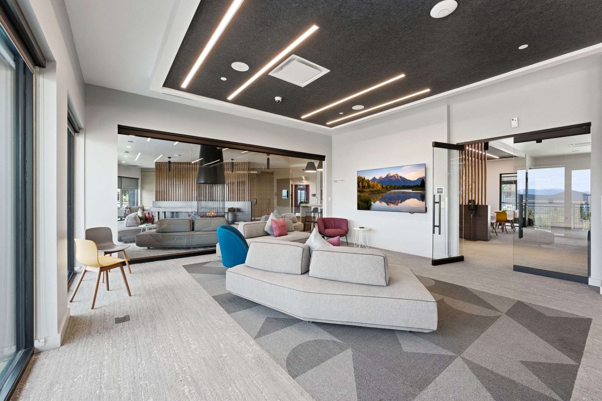 Open-concept common area featuring a geometric carpet design, a dark acoustic ceiling with linear lighting, and large glass partitions