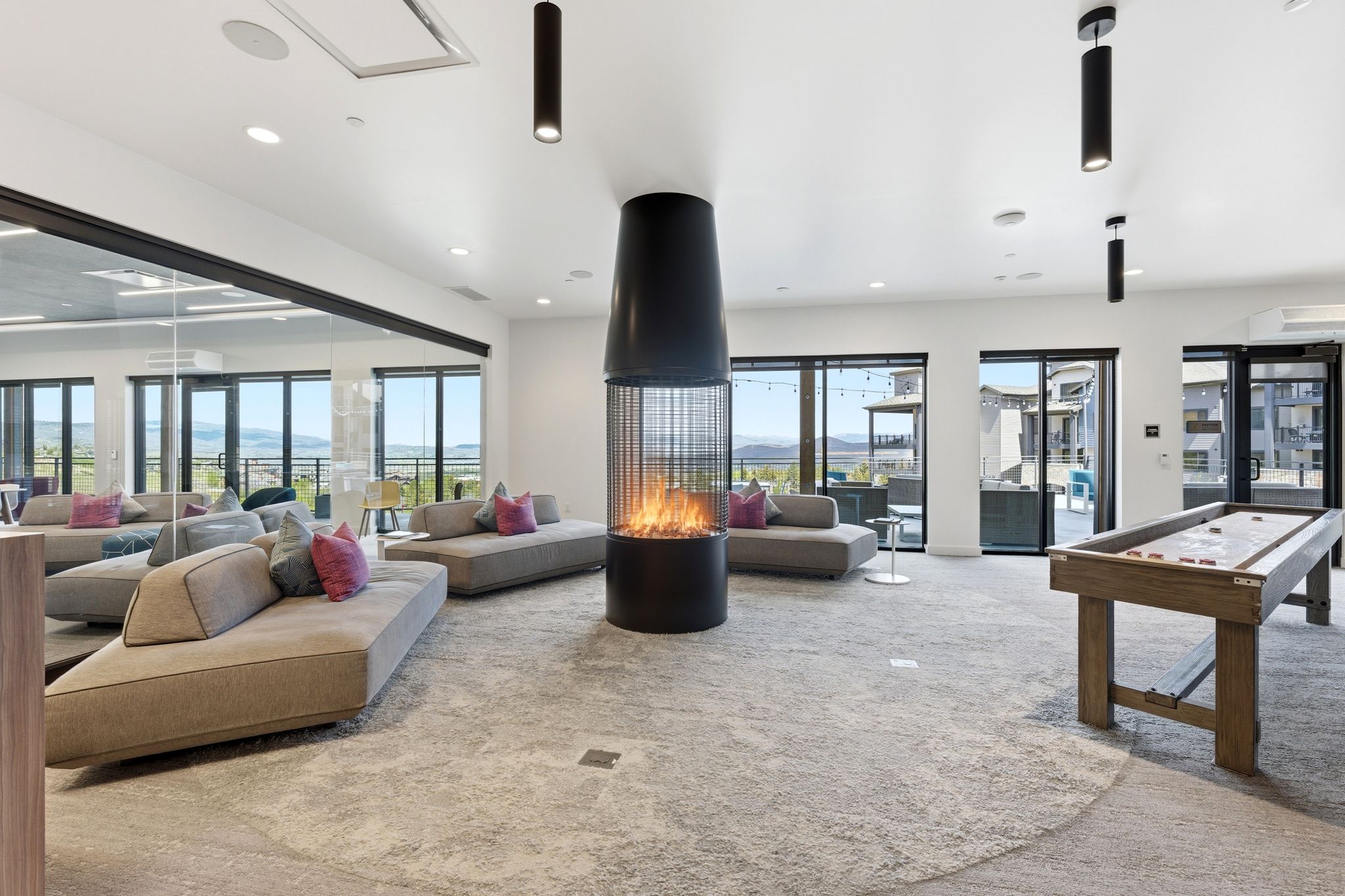 Spacious common area featuring a modern fireplace, neutral-toned carpet, and a shuffleboard table