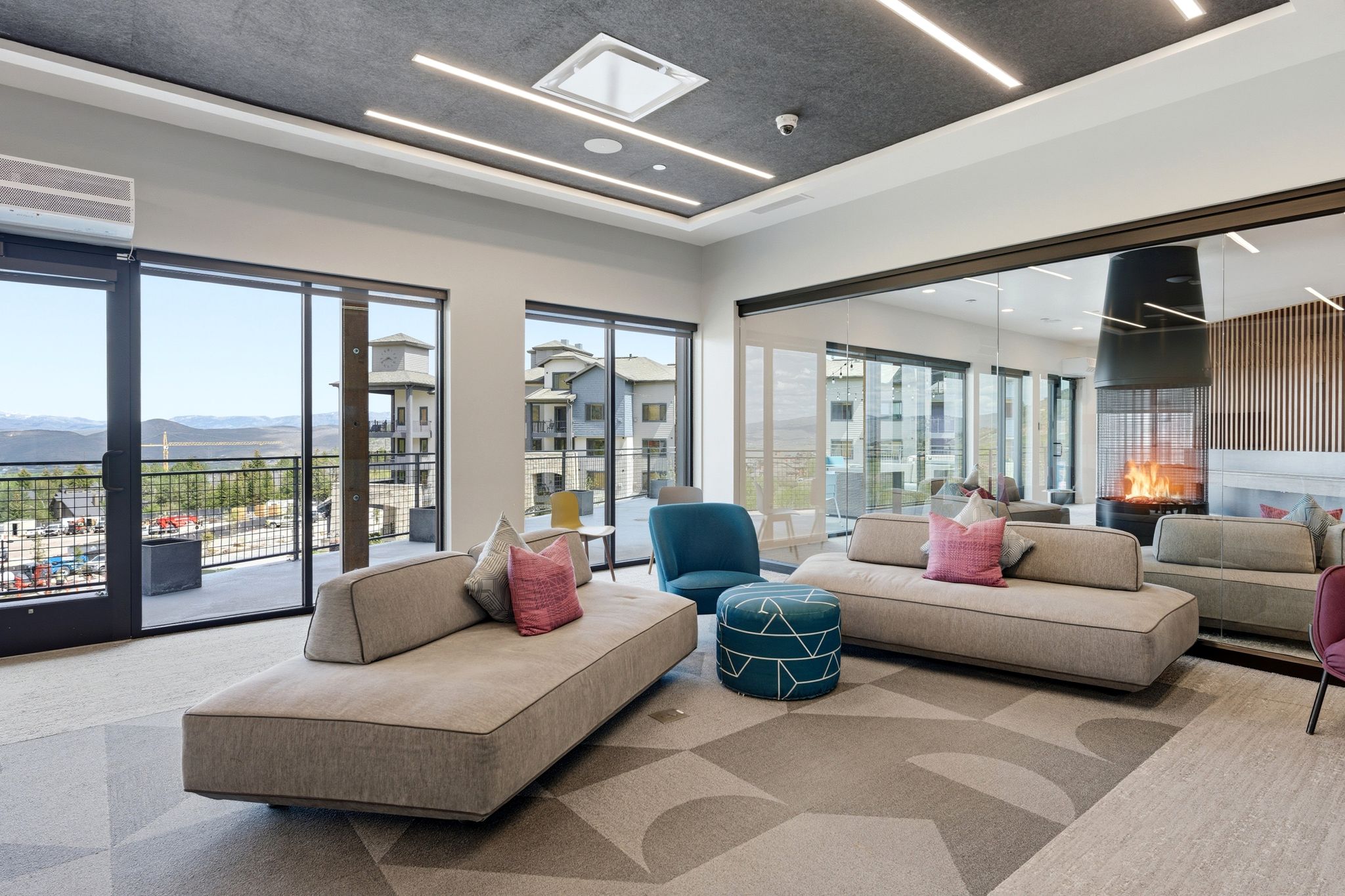 Spacious interior featuring a contemporary ceiling-mounted fireplace, floor-to-ceiling windows, and a large glass-paneled door opening to a private balcony