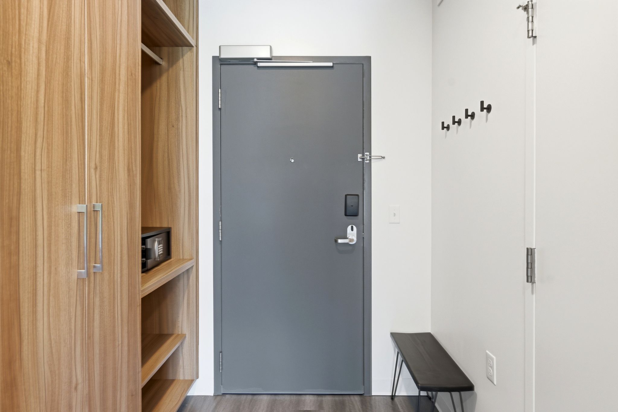 Entryway featuring a grey door with a digital lock, wood-finish cabinetry with silver hardware, integrated shelving, and a wall-mounted coat rack