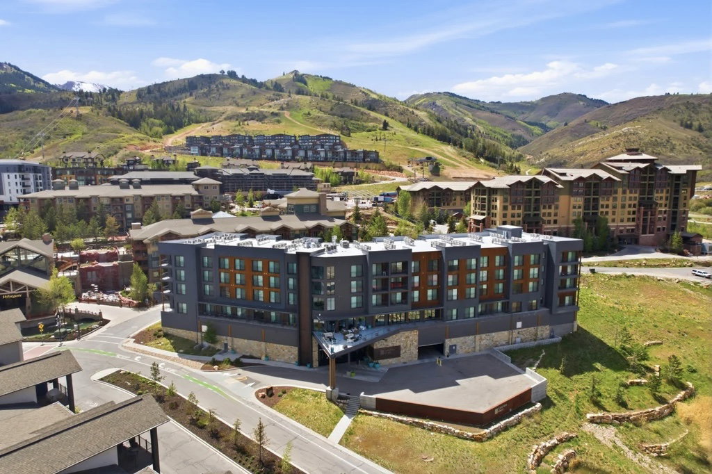 Modern multi-story building featuring stone and wood-finish paneling, multiple balconies, and a paved entrance