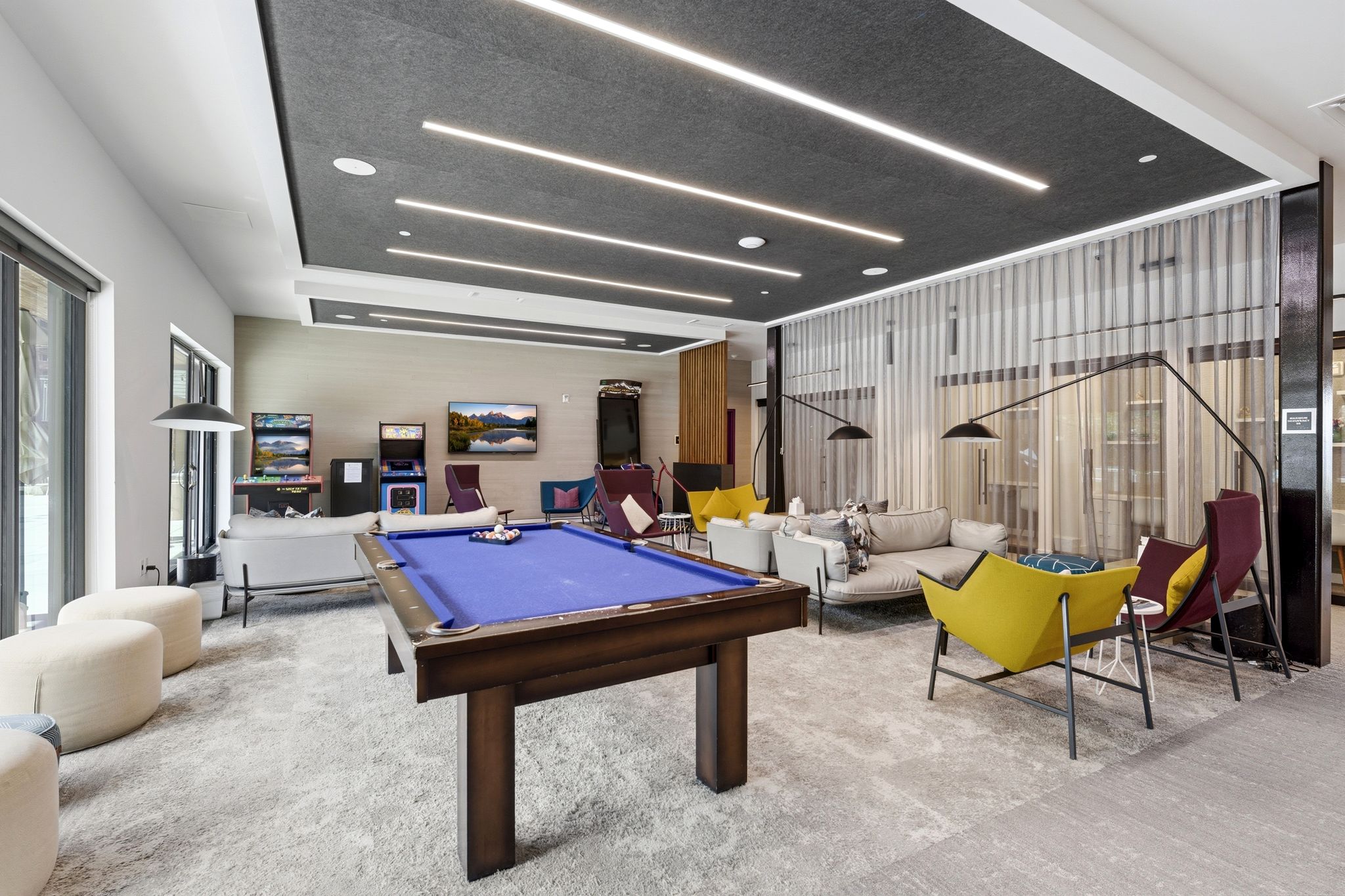 Spacious recreation room featuring a billiards table, wall-mounted display screens, and a grey acoustic panel ceiling with linear lighting
