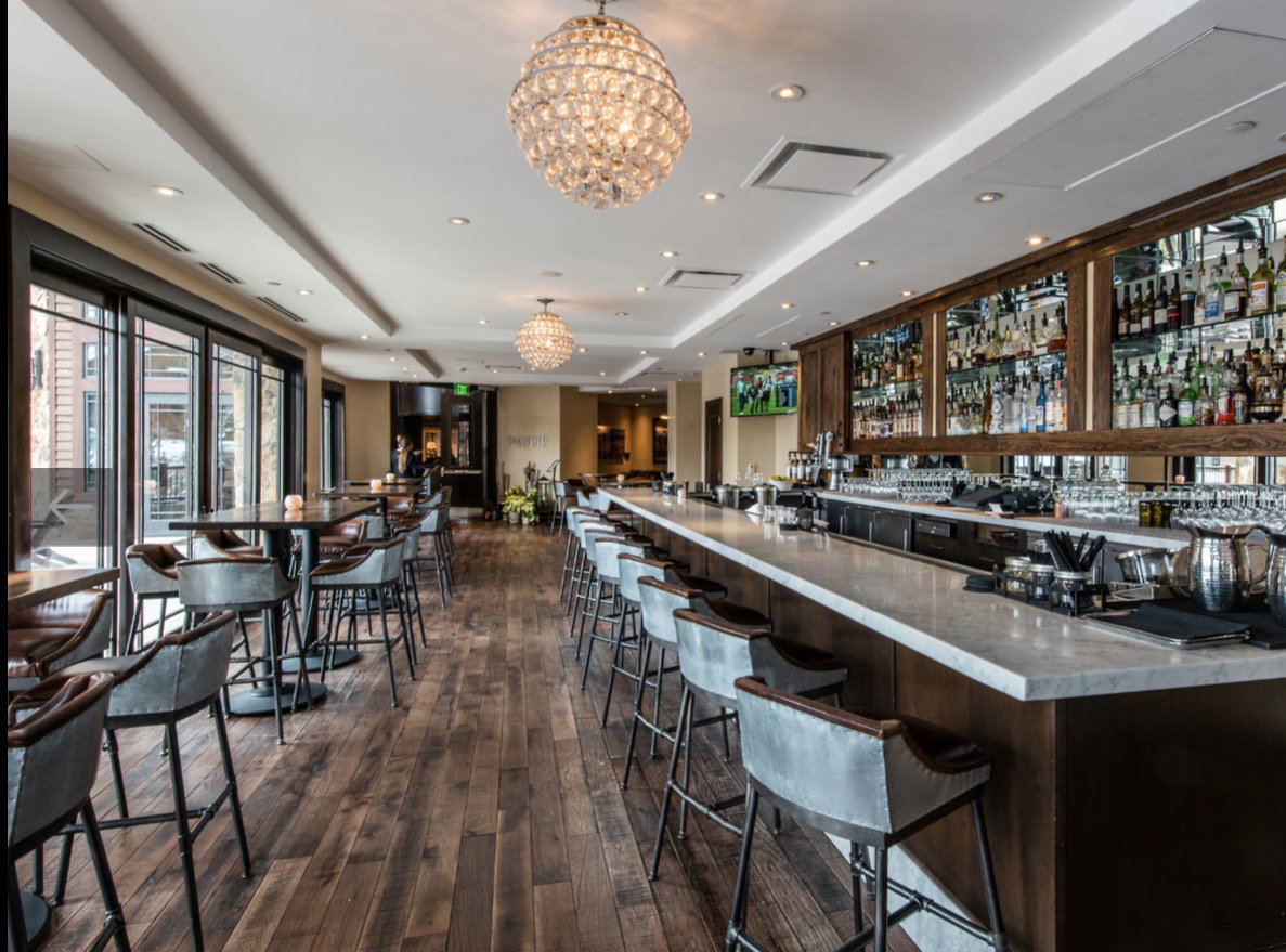 Expansive bar area featuring a long stone-top bar, wood-finish flooring, and multiple crystal chandeliers