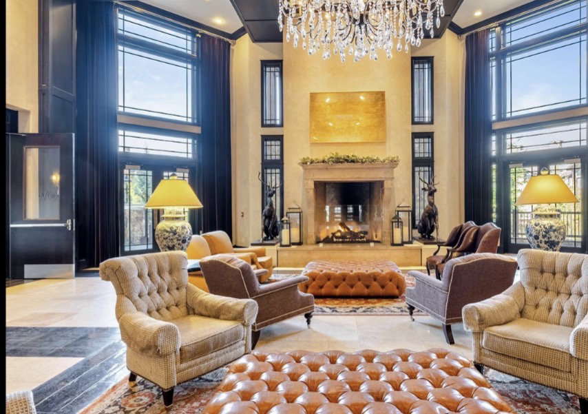 Grand sitting area featuring a prominent fireplace with a stone surround, tall windows with transom detailing, and a multi-tiered crystal chandelier