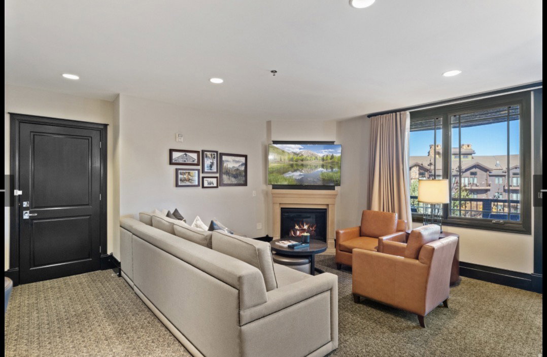 Living area featuring patterned carpet flooring, a corner fireplace with a mantel, recessed lighting, and a large multi-pane window