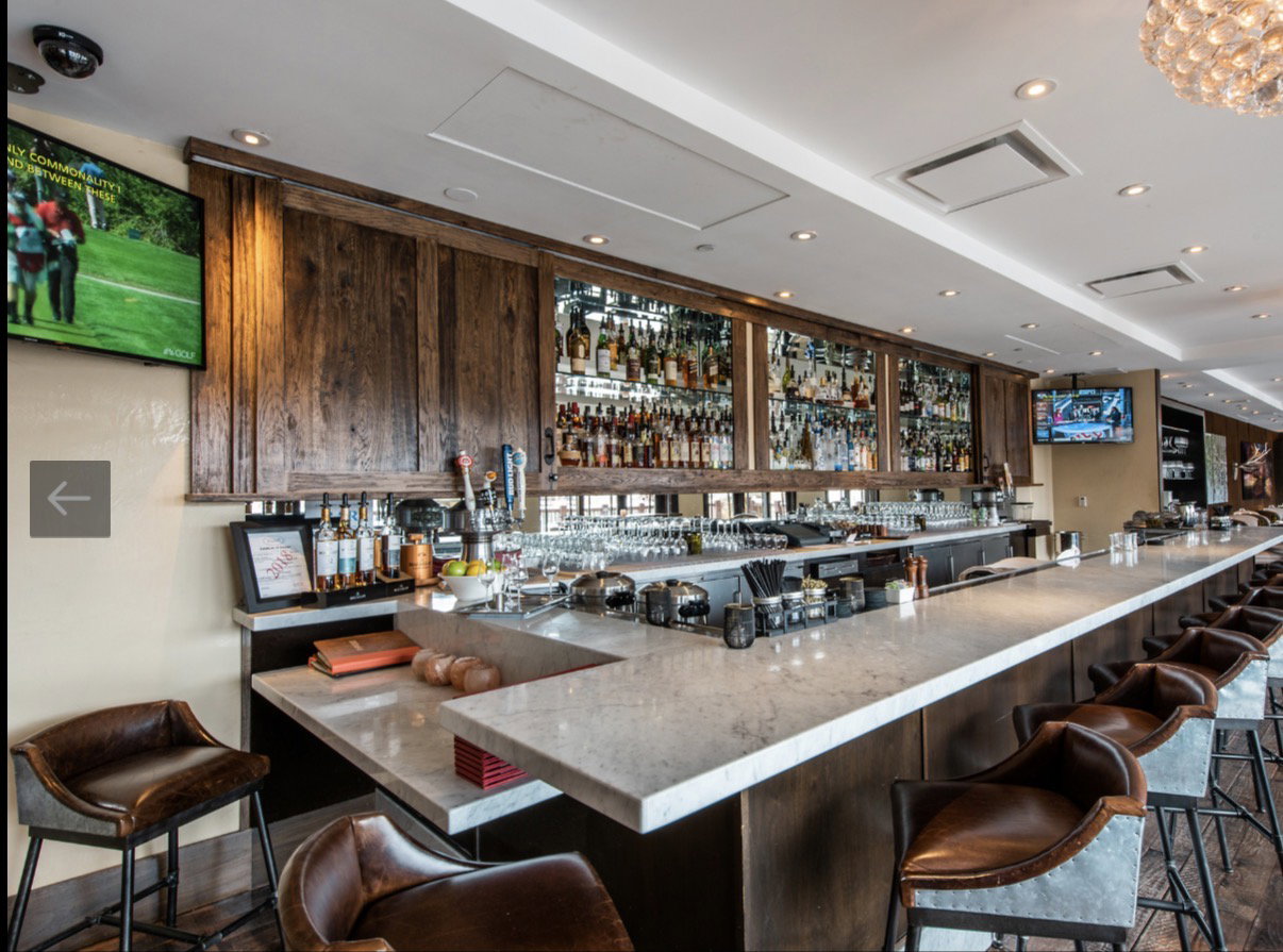 Expansive bar area featuring a light-toned countertop, integrated shelving with mirrored backing, recessed lighting, and wood-finish paneling