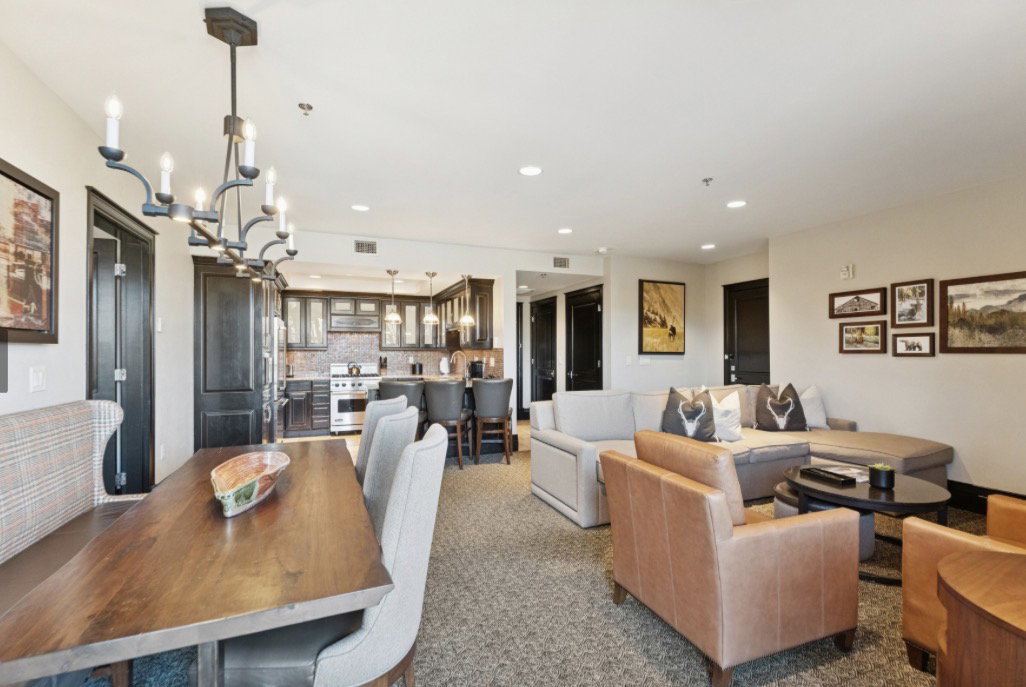 Open-concept living space featuring a dining area with a dark wood table, an overhead chandelier, and a kitchen with dark cabinetry and stainless steel appliances