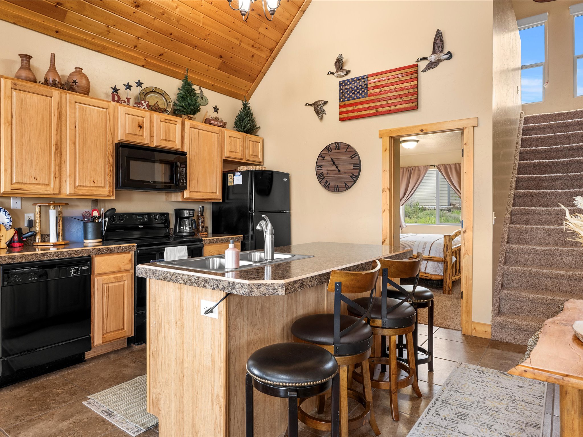 Kitchen featuring light wood cabinetry, black appliances, a stone-finish countertop, and a double-basin sink