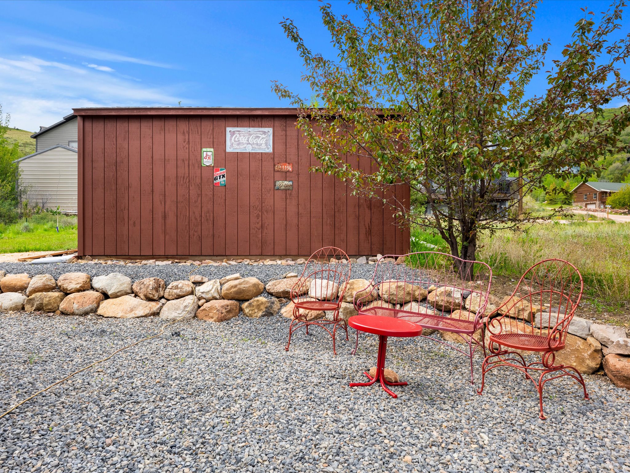 Freestanding shed with horizontal wood siding, gravel ground cover, and a natural rock retaining wall