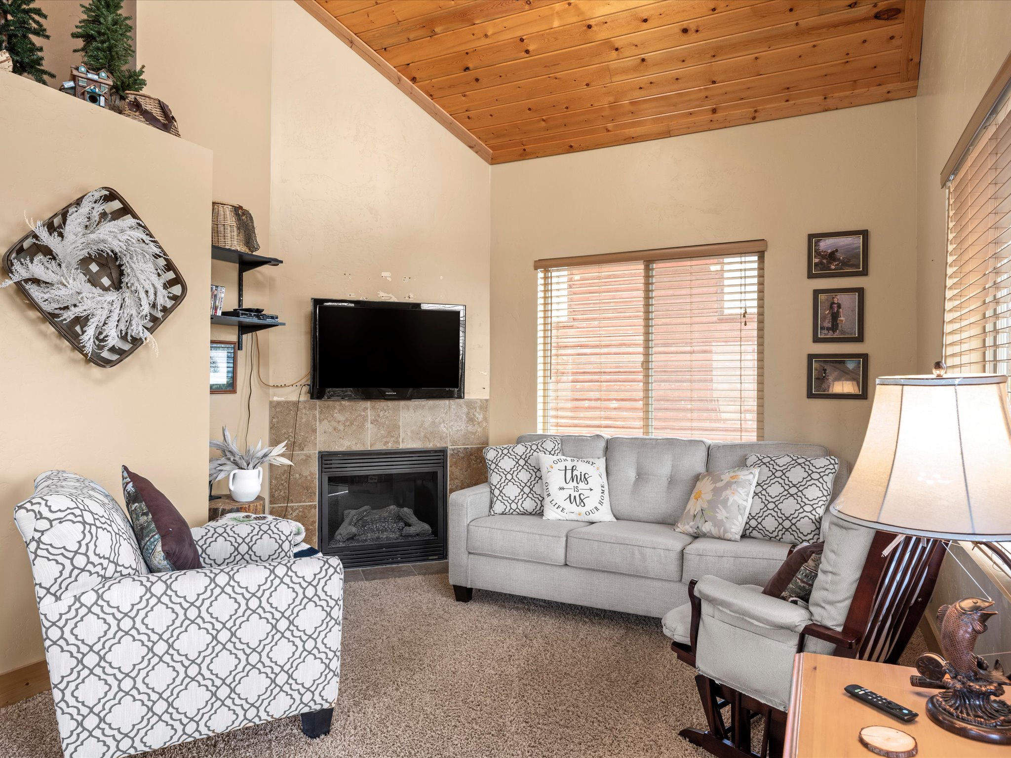 Living area featuring a vaulted wood-finish ceiling, wall-mounted television, tiled fireplace, and carpeted flooring