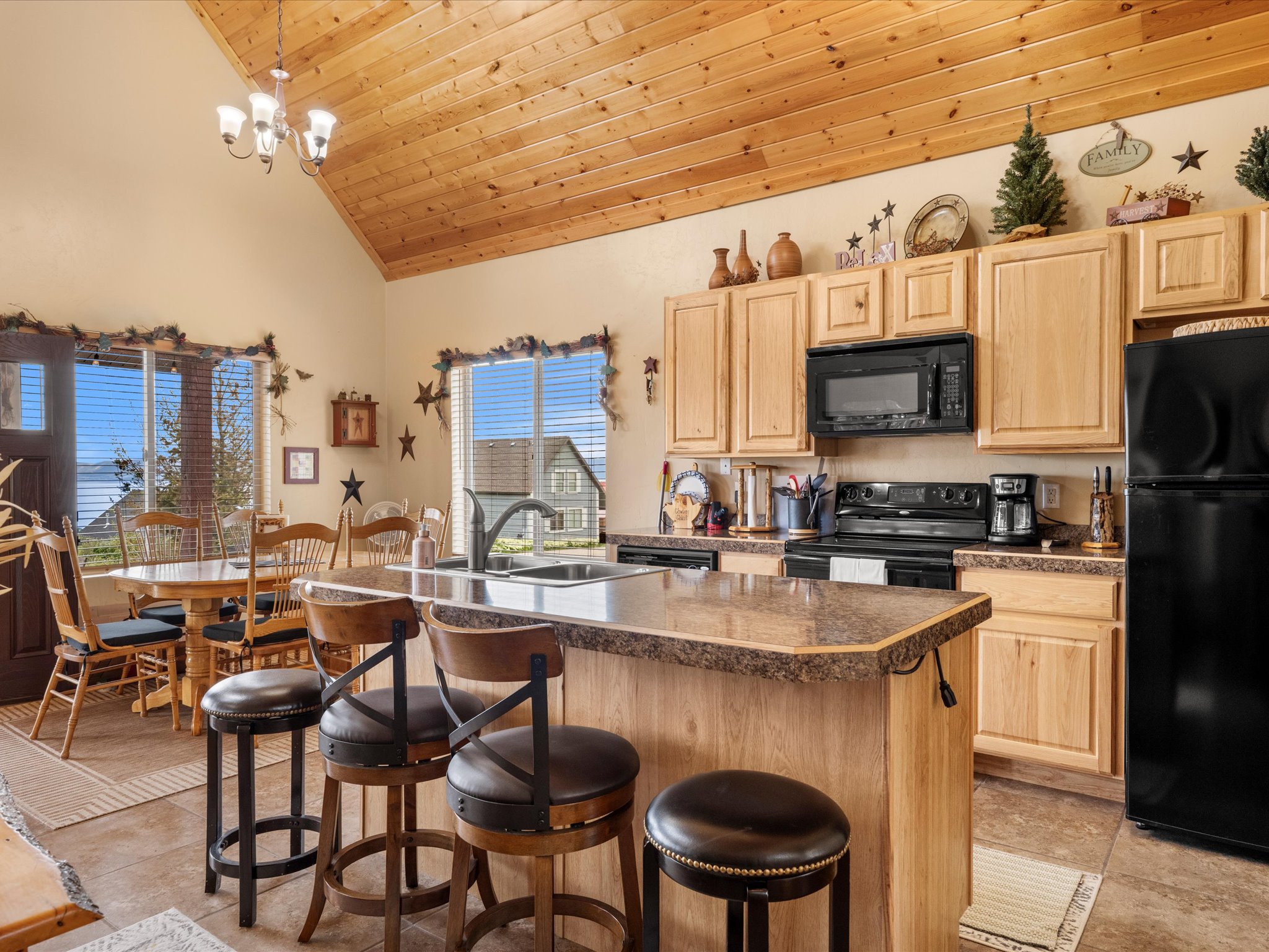Kitchen featuring wood-finish cabinetry, black appliances, a central island with an integrated sink, and an exposed wood plank vaulted ceiling