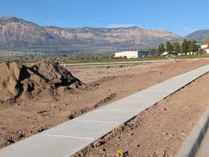New concrete sidewalk and curb in a developing area, framed by expansive mountain scenery
