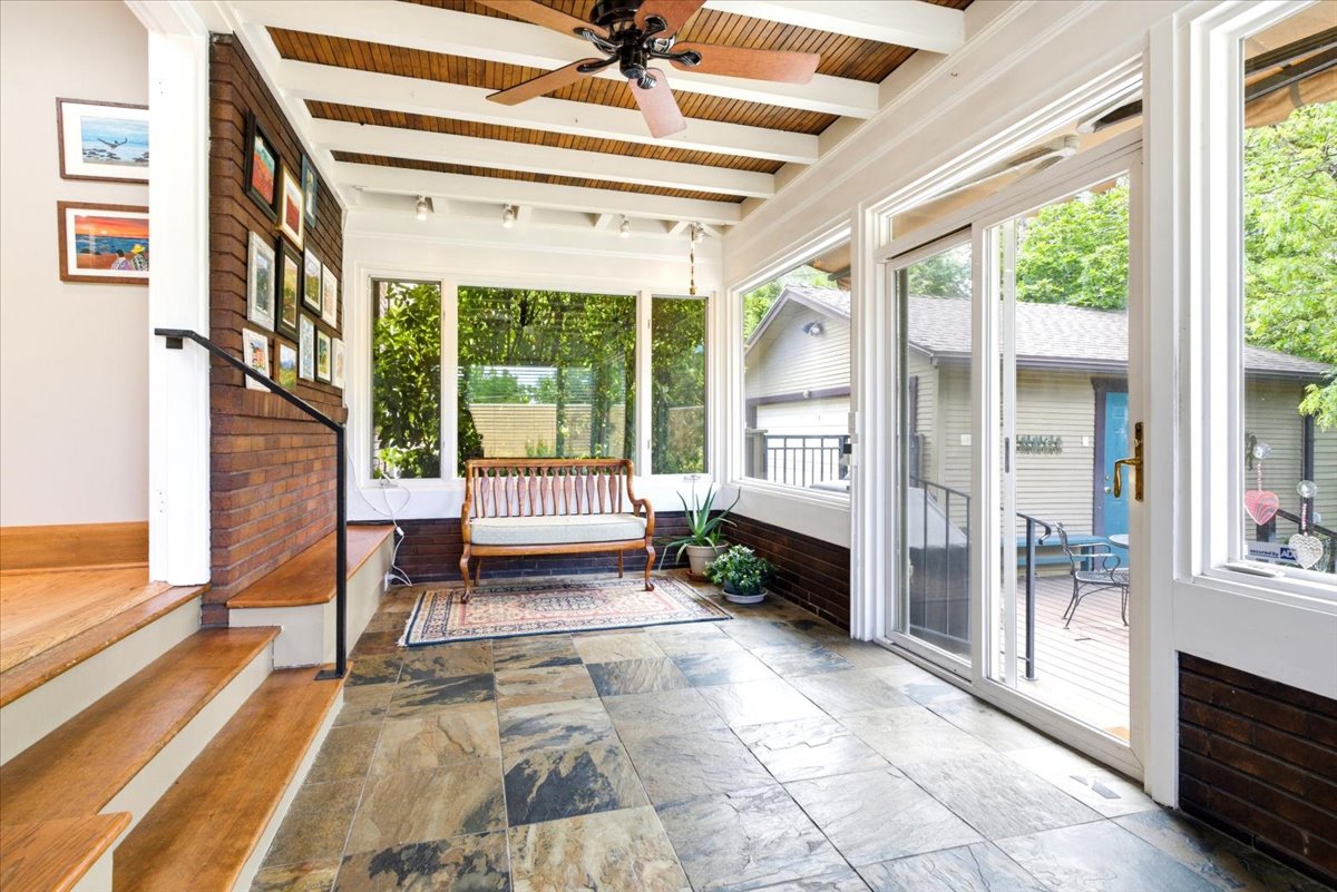 Enclosed porch featuring slate tile flooring, exposed wood beam ceiling, brick wall detailing, and abundant natural light from multiple windows