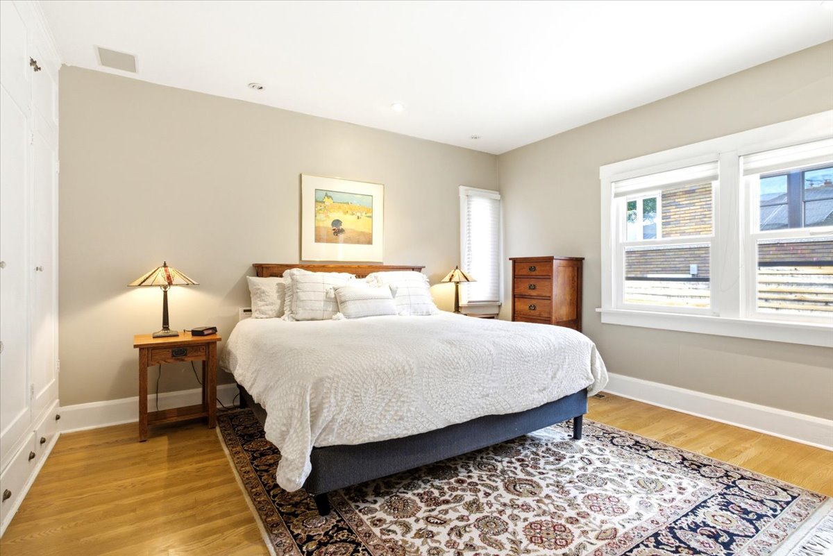 Bright room featuring wood-finish flooring, two large windows with white trim, recessed lighting, and built-in white cabinetry
