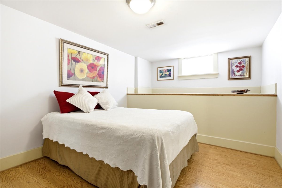 Recessed bedroom featuring light wood-finish flooring, a neutral color palette, a ceiling-mounted light fixture, a built-in half-wall partition, and a single transom window