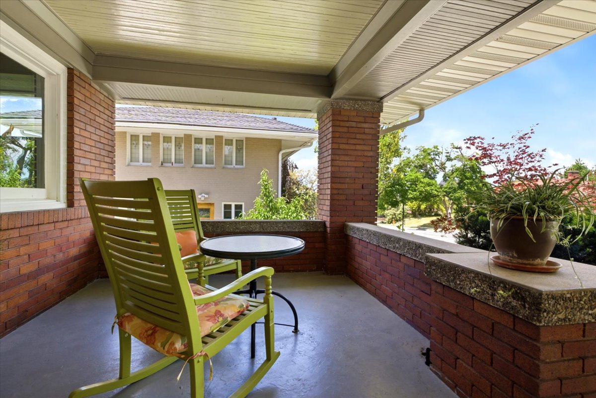 Covered front porch featuring brick columns and knee wall, concrete flooring, and a white soffit ceiling
