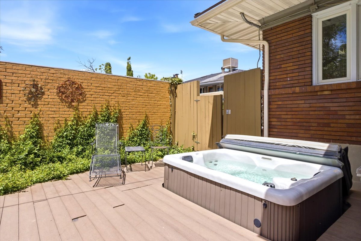 Private patio featuring a built-in hot tub, composite decking, and a brick privacy wall adorned with climbing greenery