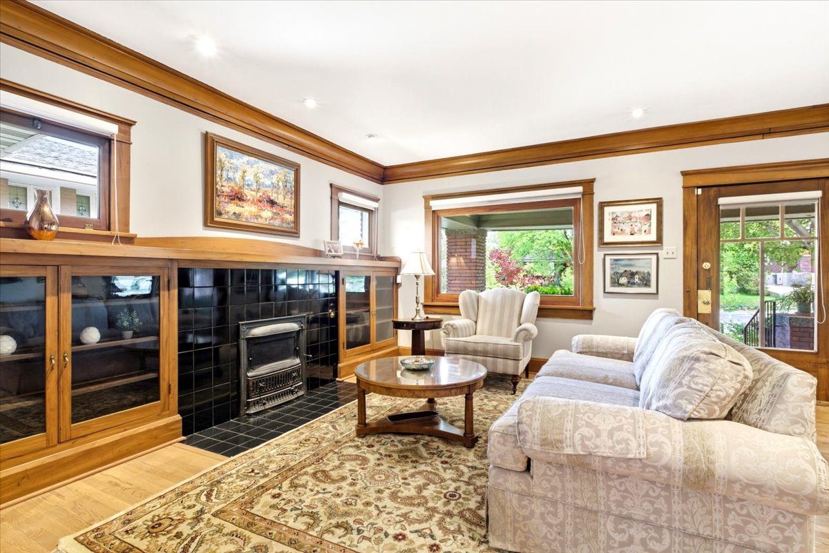 Living area featuring extensive wood trim, built-in cabinetry with glass fronts, a tile-surround fireplace with a decorative cast-iron insert, and wood-finish flooring