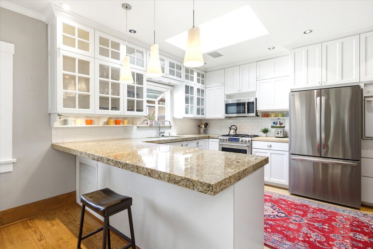 Bright kitchen featuring white cabinetry, a U-shaped countertop with a granite finish, and stainless steel appliances