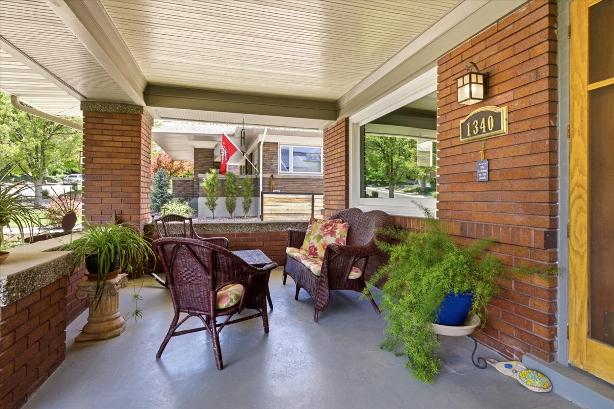Covered front porch featuring brick columns and wall details, a large picture window, and a wall-mounted exterior light fixture