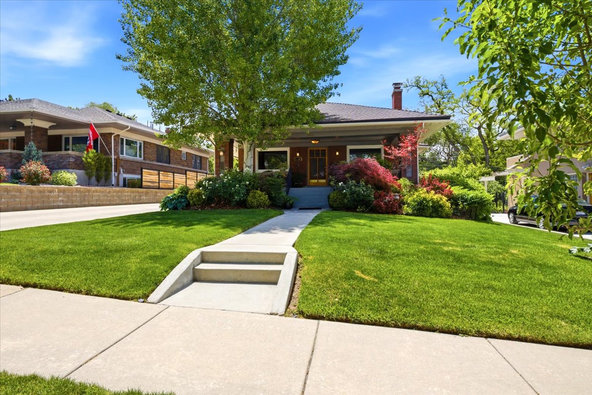 Craftsman-style residence featuring a prominent front lawn, concrete pathway with steps, and mature landscaping